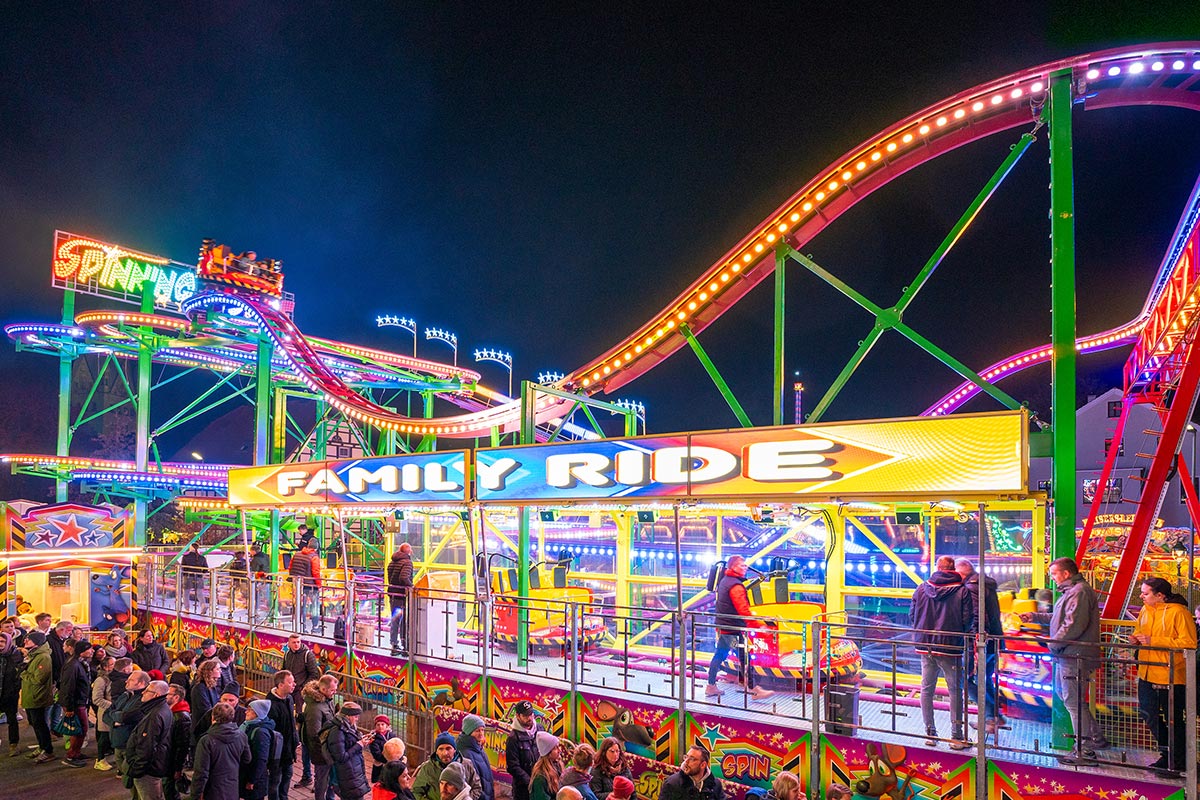 Die rasante Volksfest-Achterbahn Spinning Mouse bei abendlicher, farbenfroher Beleuchtung