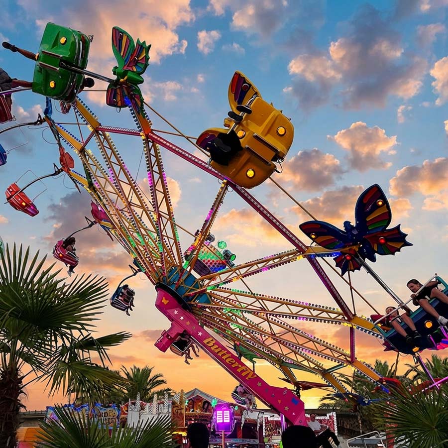 Ein sommerlicher Blick auf ein Fahrgeschäft bei er Dresdner Vogelwiese mit sonnigem Himmel und Palmen