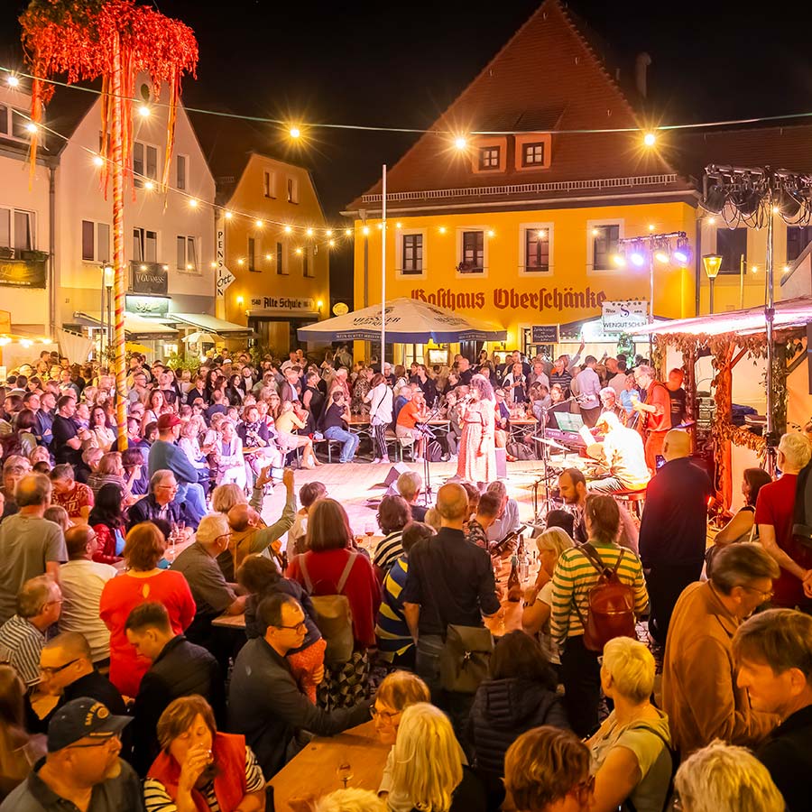 Ein gut gefüllter Marktplatz am Abend, wo viele Menschen zum Weinfest in Radebeul gesellig zusammensitzen.